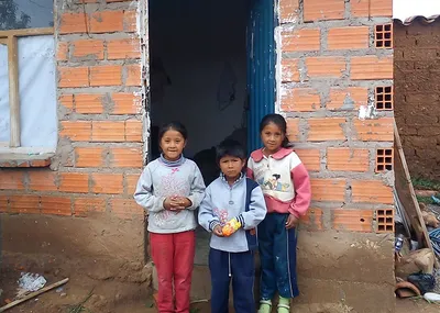 Drei Kinder vor einem unverputzen Haus